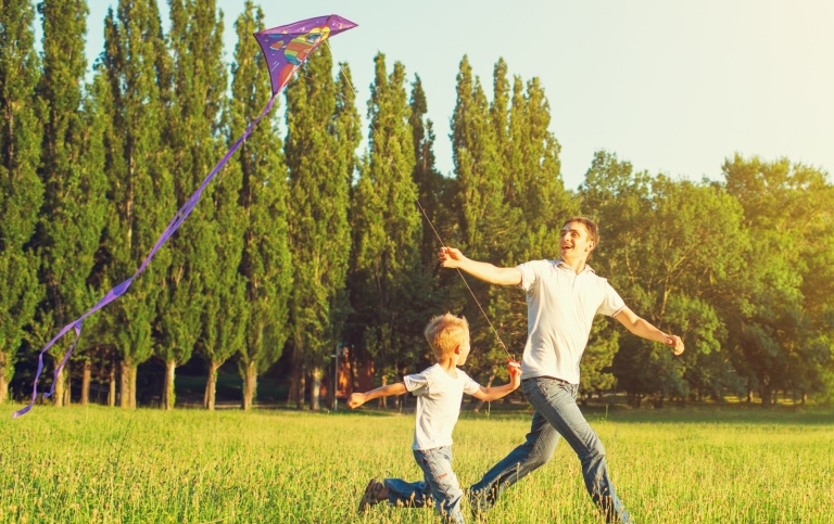 Man och pojke springer över äng med drake