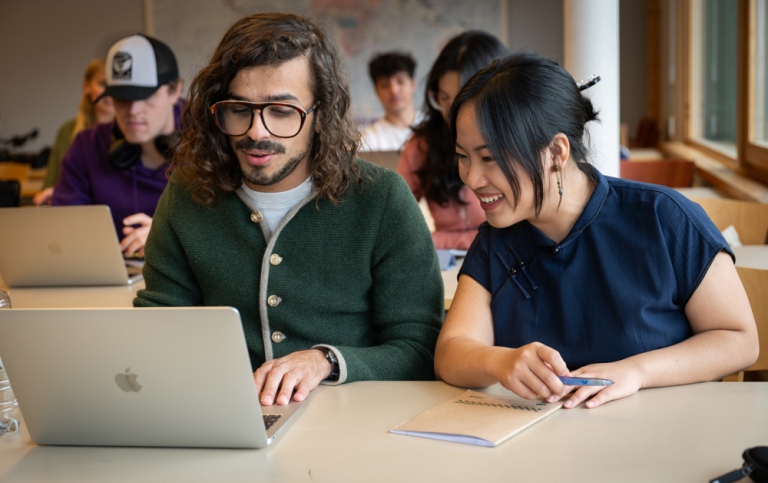 Två studenter framför en dator i en föreläsningssal.